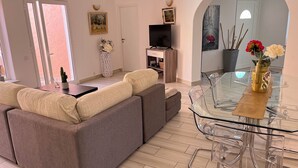 Un salon moderne avec un canapé gris, une table à manger en verre et des chaises transparentes.