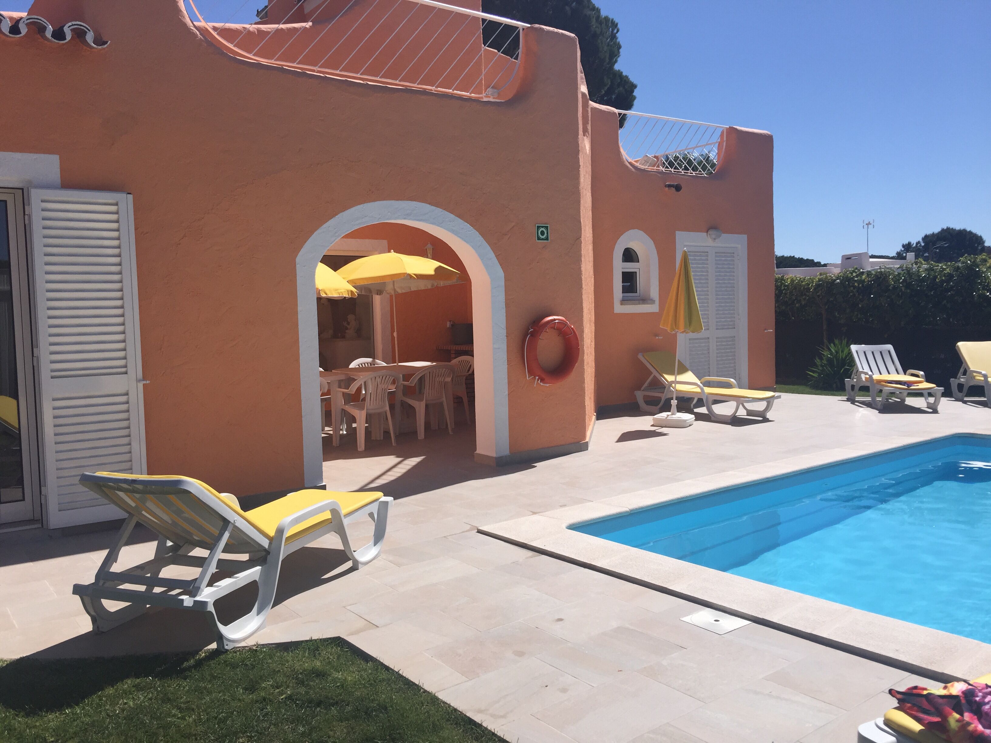 A poolside area with lounge chairs, a dining area with tables and chairs, and a lifebuoy on the wall.
