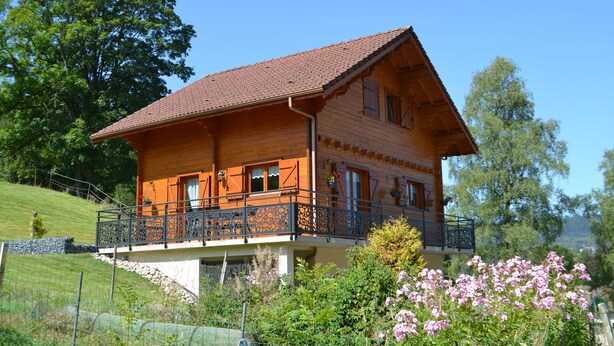 A wooden chalet with a balcony, surrounded by greenery and flowers.