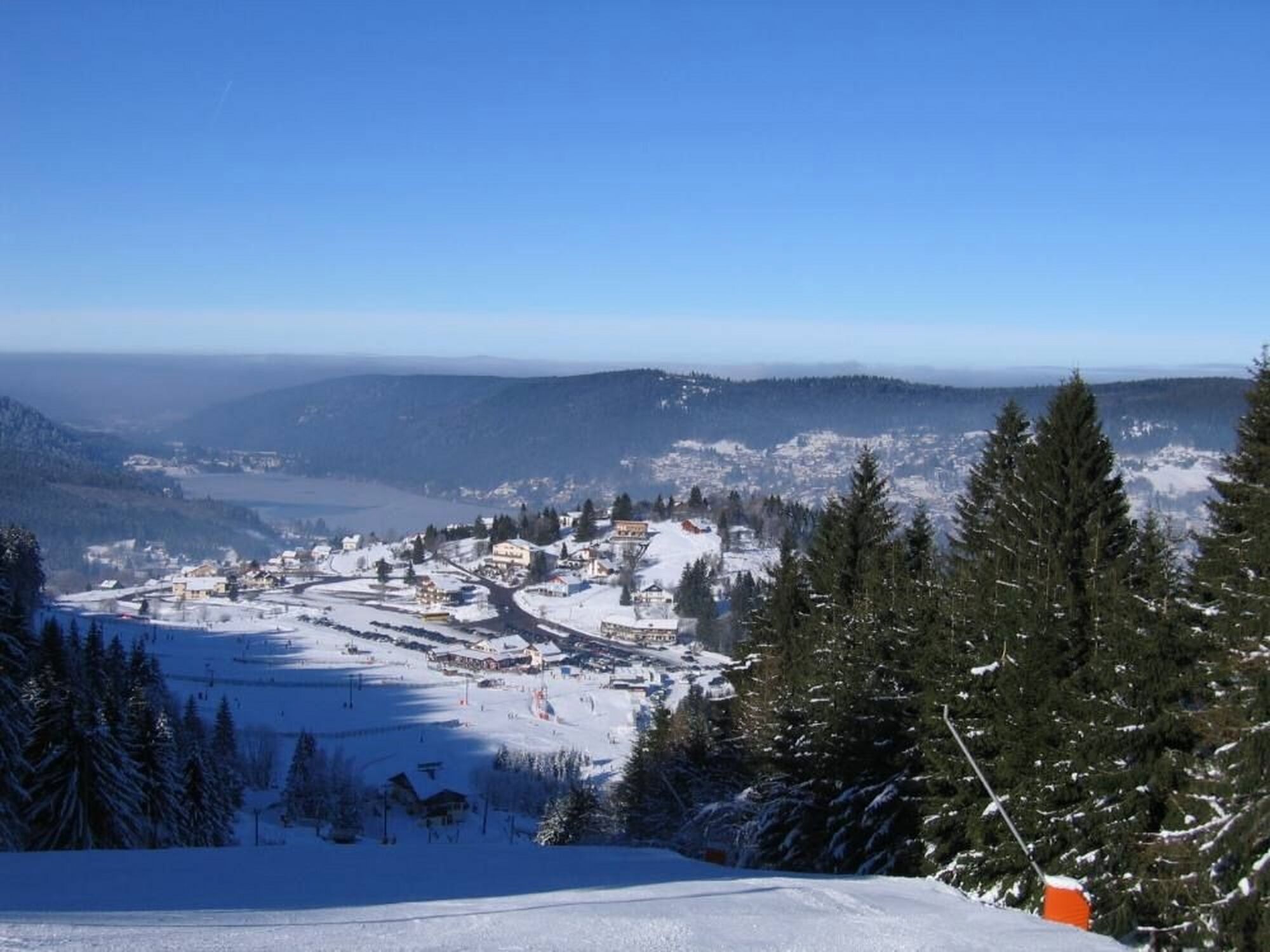 Une ville de montagne enneigée, avec des bâtiments, des pistes de ski et une forêt dense.