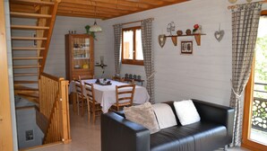 A cozy room with a black leather sofa, wooden dining table, and a staircase leading to an upper level.