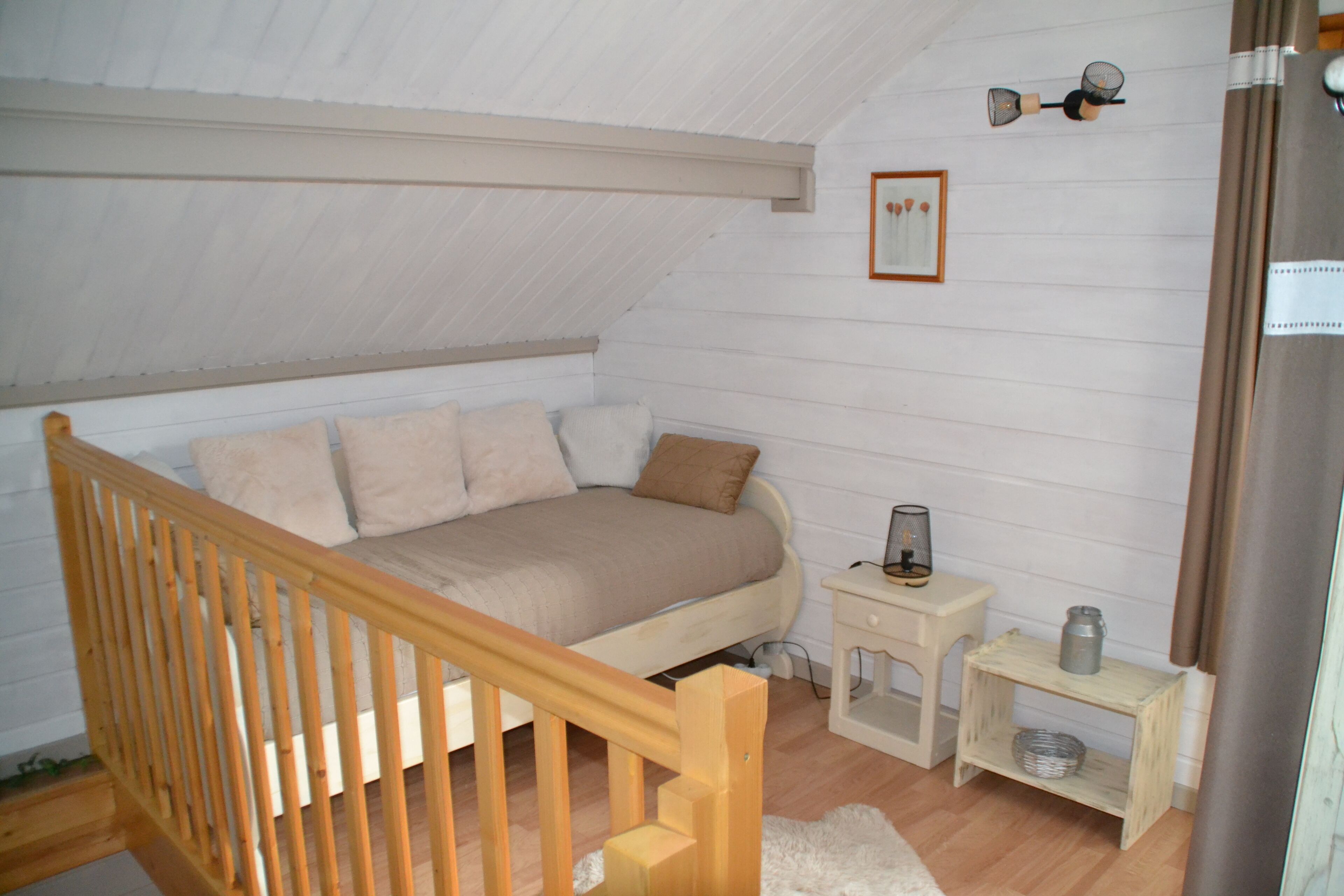 Une chambre mansardée chaleureuse, avec un lit en bois, une petite table de chevet et une commode.