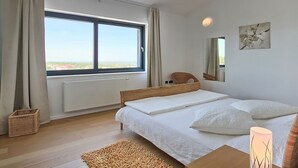 Ett sovrum med ett stort fönster, en säng, en stol, en spegel och ett konstverk på väggen.