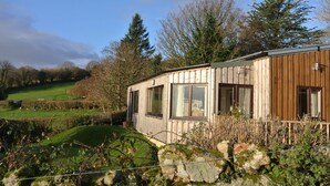 Eine Holzhütte mit großen Fenstern, umgeben von üppiger grüner Landschaft und Bäumen.
