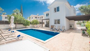 Ein Swimmingpool mit Liegestühlen und Sonnenschirmen, umgeben von einem weißen Gebäude mit einem Ziegeldach.