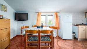 A compact kitchen with a dining table, chairs, a TV, a refrigerator, and a window with curtains. - ALEKS house with apartments / Aleks 2 APARTMENT (Umag)