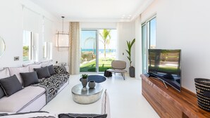 Een moderne woonkamer met een bank, salontafel, televisie en grote ramen met uitzicht op een tuin.