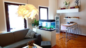 Ein Wohnzimmer mit einer Couch, einem kleinen Tisch mit Pflanze, einem Aquarium und einem Essbereich mit Stühlen.