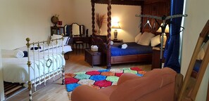 A bedroom with a four-poster bed, a smaller single bed, a wooden nightstand, a desk, and a colorful hexagonal rug.