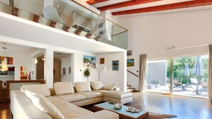 Un vaste espace de vie comprenant un grand canapé en forme de L, une table basse et une balustrade en verre donnant sur un balcon.