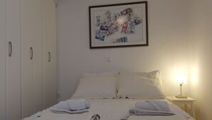 Una camera da letto con un letto, cuscini, un comodino con una lampada e un quadro appeso al muro.