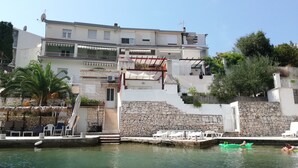 Un edificio costiero con facciata in pietra, un balcone e una zona piscina con lettini.