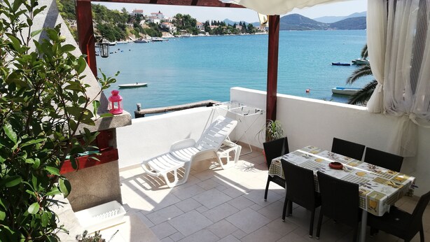 Una terrazza con tavolo e sedie, vista su uno specchio d'acqua con imbarcazioni.