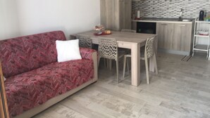 A modern kitchen with a dining area, featuring a red patterned sofa, a wooden dining table, and a kitchen counter.