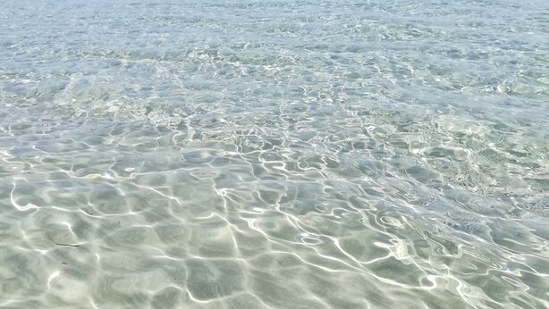 Clear shallow waters with visible sand patterns and a distant shoreline.