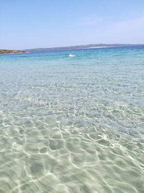 Clear shallow waters with visible sand patterns and a distant shoreline.