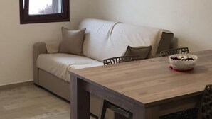 A small, modern living space with a sofa, a dining table, and a window with curtains.