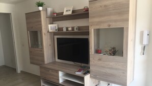 A modern living room with a built-in entertainment unit, wooden flooring, and a large flat-screen TV.