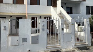 A multi-story building with a white exterior, a gated entrance with a metal gate, and a staircase leading to the upper floors.