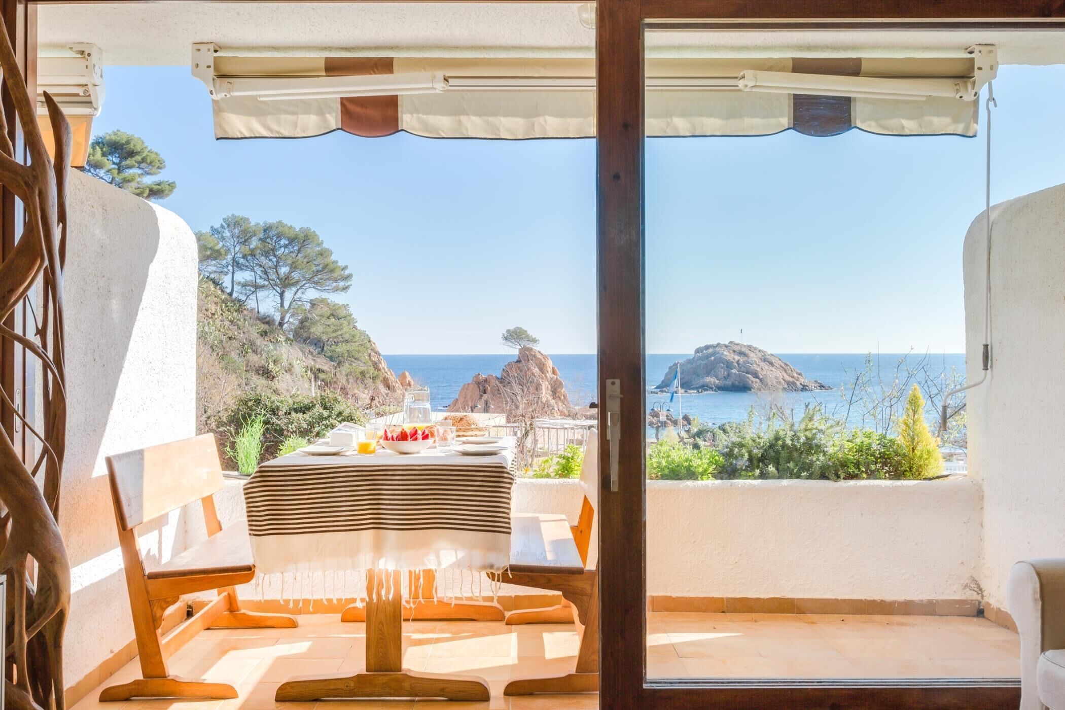 Un balcon avec une table dressée pour le dîner, offrant une vue sur un paysage côtier caractérisé par des affleurements rocheux et la mer.