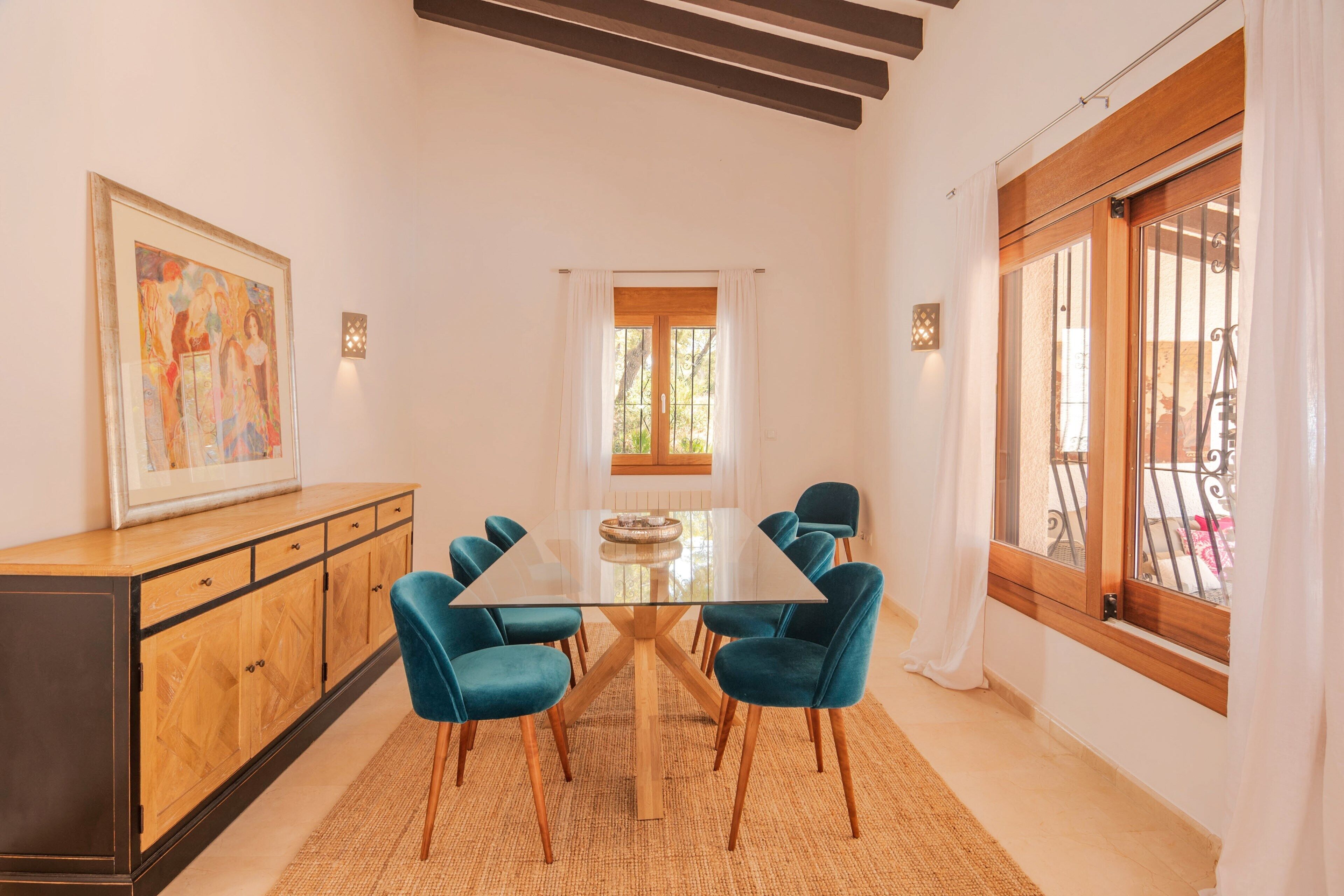 A dining area with a glass-top table surrounded by six chairs, a wooden cabinet, and a large painting on the wall.