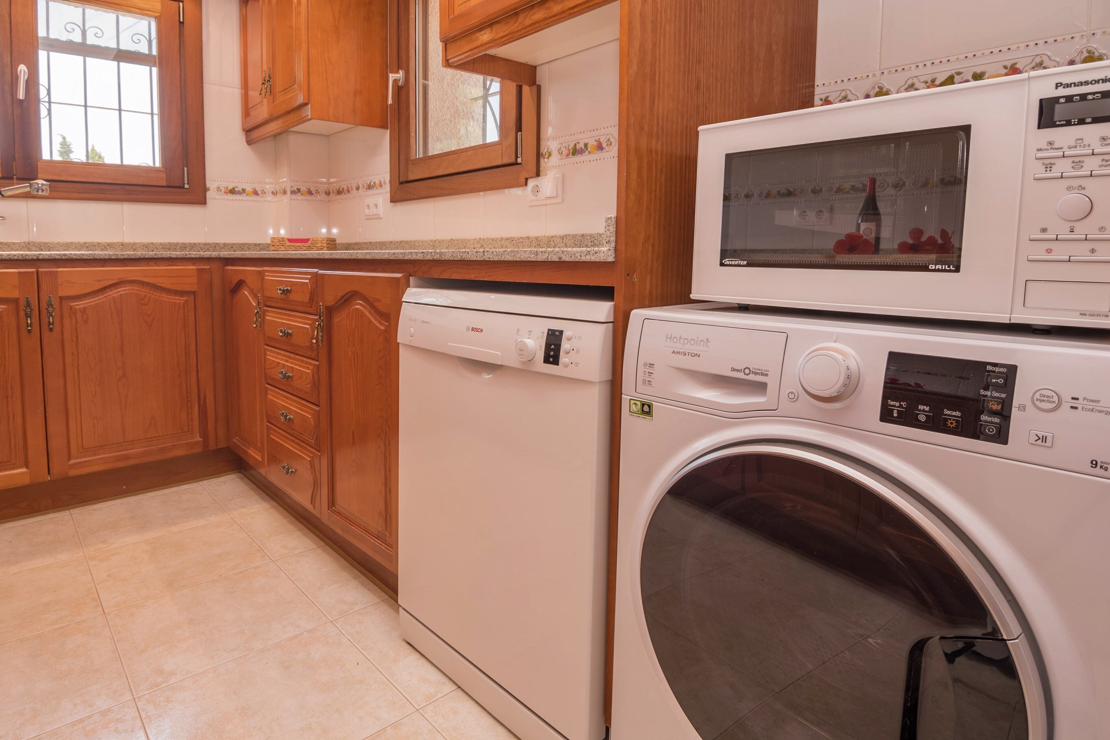 Une cuisine dotée de meubles en bois, d’un lave-vaisselle Bosch, d’une machine à laver Hotpoint et d’un gril Panasonic.