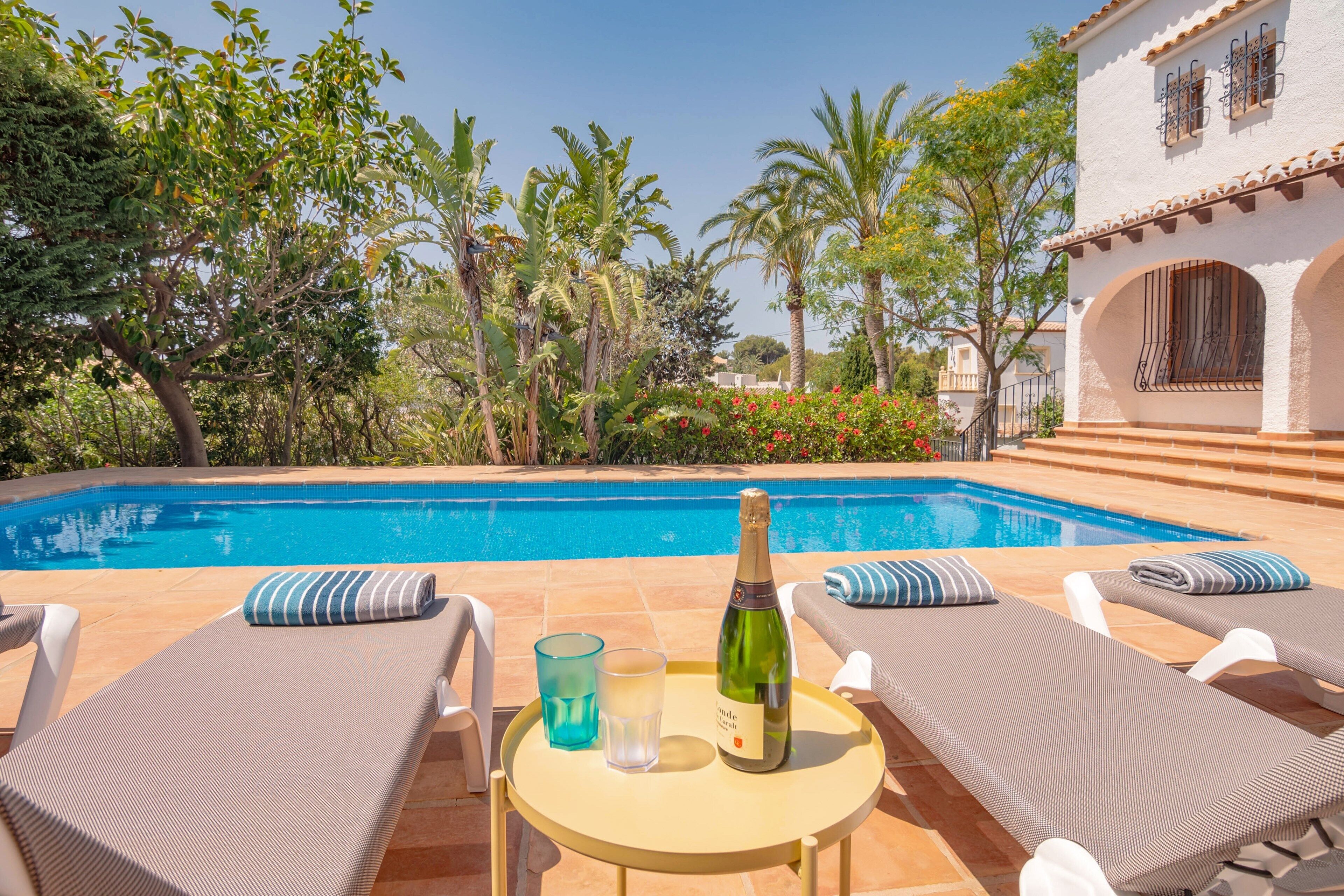 A poolside area with lounge chairs, a table with a bottle and glasses, and a clear view of the pool.