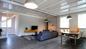 A modern living room with a grey sofa, a TV, and a dining area with a table and chairs.