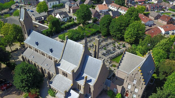 An aerial view of a historic building with a large courtyard, surrounded by trees and adjacent residential buildings.