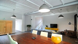 A spacious living area with a wooden dining table, grey sofas, and a TV on a yellow shelf.