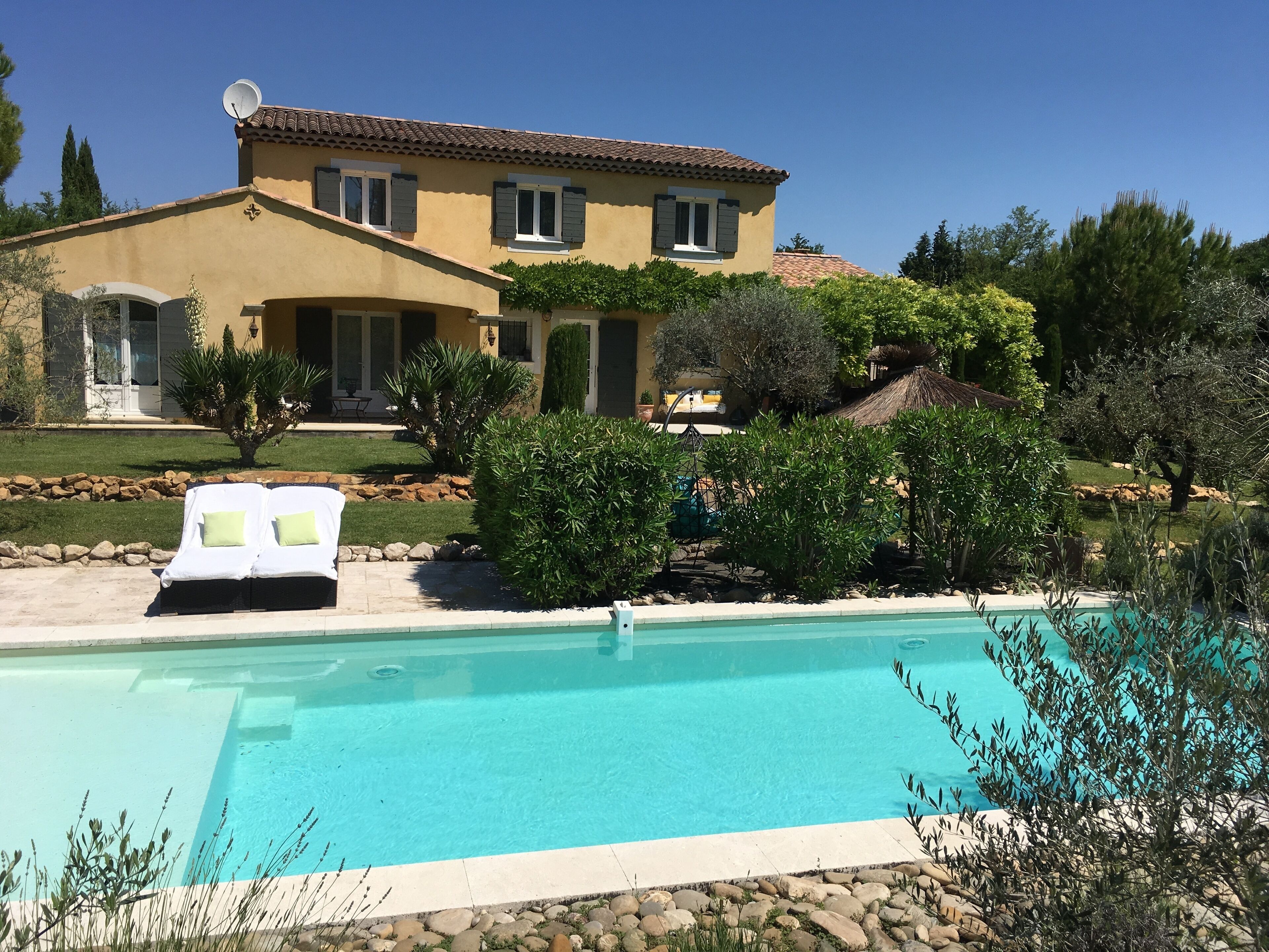 Une maison à deux étages avec une piscine, entourée de verdure et dotée d’une pelouse bien entretenue.