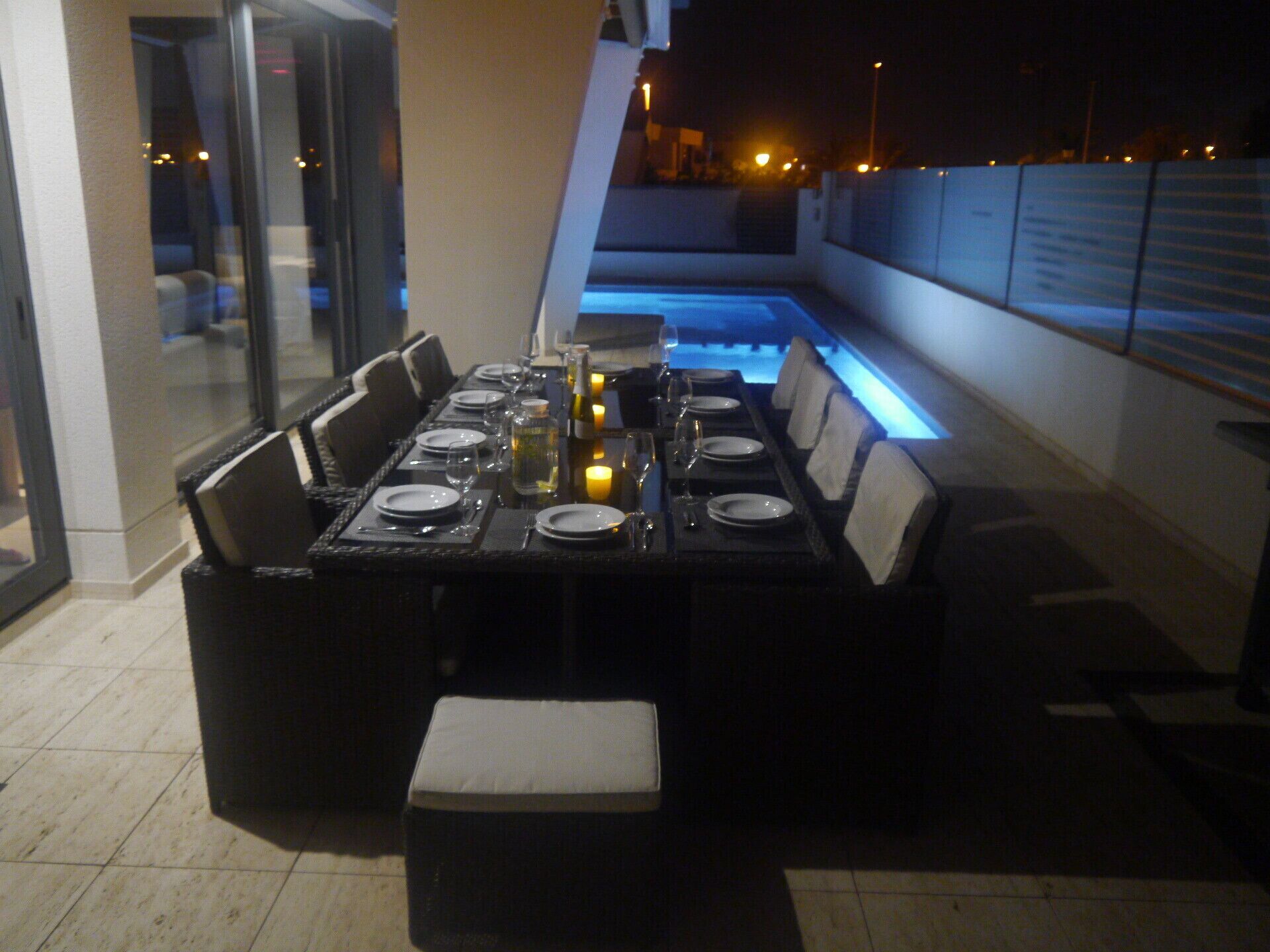 Un coin repas avec une longue table dressée pour quatre personnes, agrémenté de chaises noires, d’assiettes blanches et de bougies.