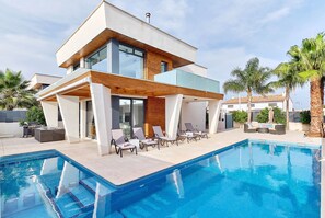 Et moderne hus med to etager, en swimmingpool, udendørs siddepladser og et grillområde.