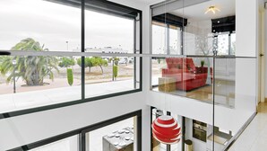 Een modern interieur met grote ramen, een rode bank en een eethoek met een opvallende rode en witte bolvormige lamp.