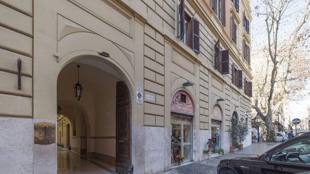A building with a large arched entrance, a sign with a number, and a shop with a pink awning.