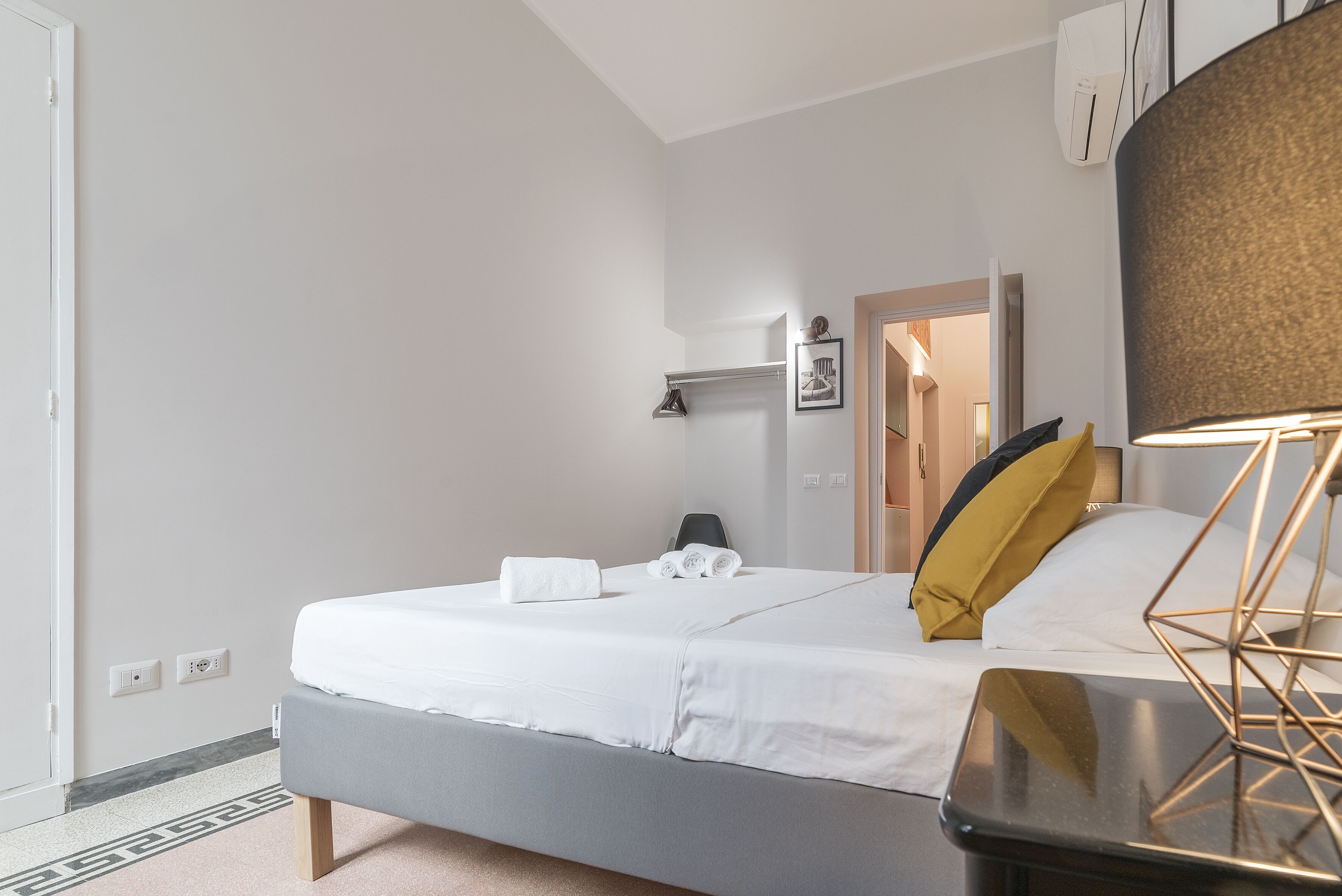 Quarto de hotel moderno com uma cama, mesa de cabeceira, abajur e espelho.
