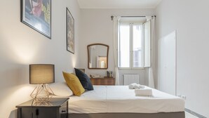 A neatly arranged bedroom with a bed, bedside lamp, dresser, and a window with curtains.