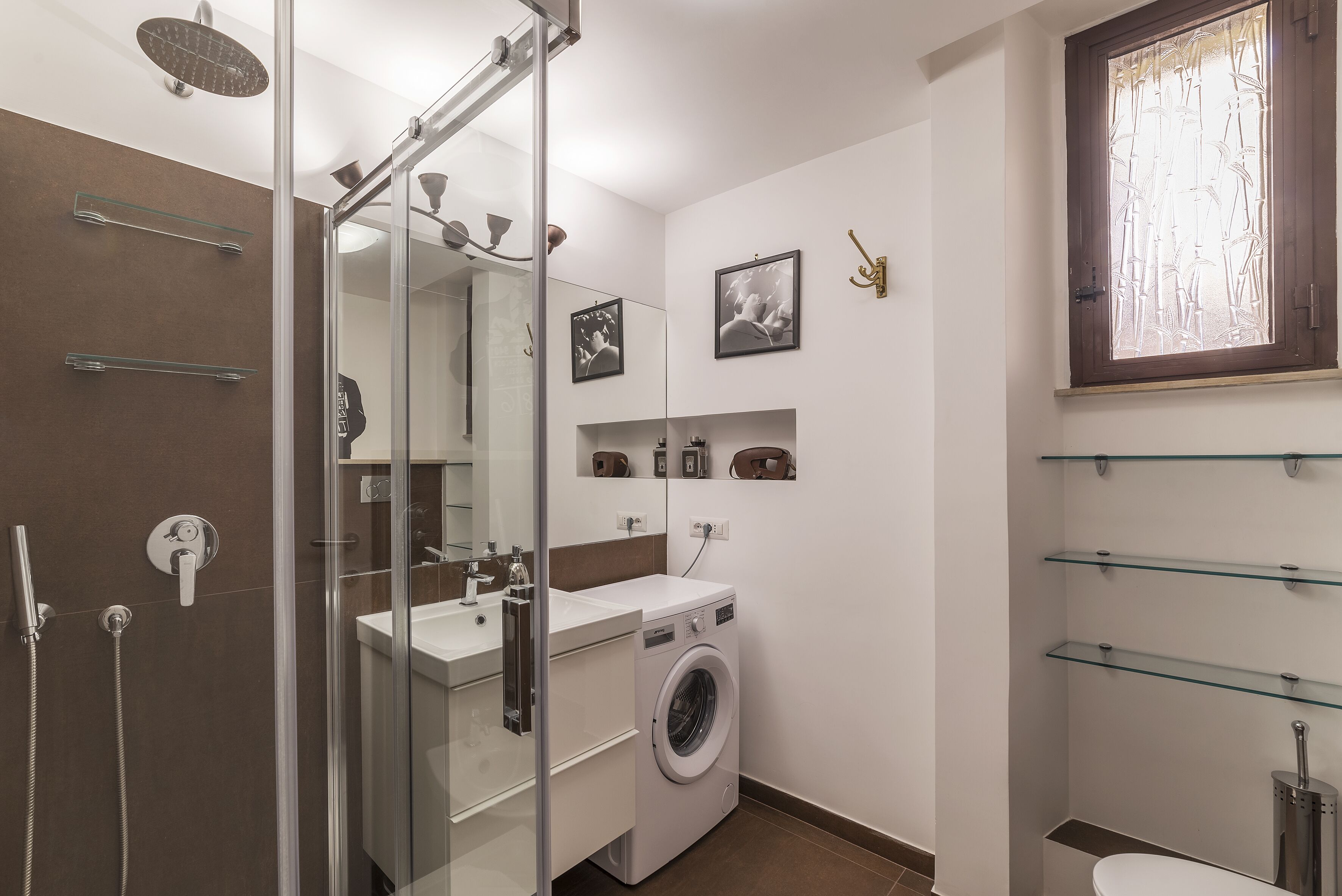A modern bathroom with a glass shower enclosure, a built-in washing machine, and a toilet.