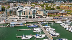 Un port de plaisance où sont amarrés de nombreux bateaux, entouré de bâtiments modernes et sous un ciel dégagé.