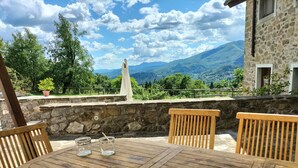 A wooden table with two chairs, a stone wall, and a view of mountains. - ✨ Luxury Tuscan Villa | Private Pool, BBQ, Wood Oven | Helicopter Tours Nearby (san romano di garfagnana (LU))