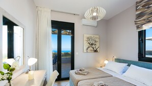Een hotelkamer met een bed, een bureau met lamp, een vaas met bloemen, een schilderij en uitzicht door de deur.