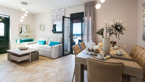 Een moderne woonkamer met een bank, salontafel en eettafel. Er is een raam met gordijnen, een spiegel en een klok aan de muur.