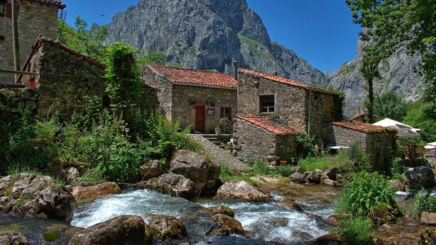 A stone building with a red-tiled roof, a small staircase leading to the entrance, and a rocky stream in front. - The Caleyon, village house with breakfast. Rooms with private bathroom. (Bulnes de Cabrales)
