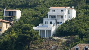 A multi-story white building with balconies, surrounded by dense greenery and other residential structures. - SPACIOUS VILLA - OWN PRIVATE POOL, WIFI,  STUNNING SEA VIEWS (Bigova)