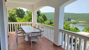 Uma área de refeições coberta ao ar livre, com mesa e cadeiras, com vista para um rio e colinas florestadas.
