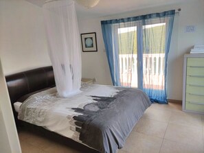 Quarto com cama, mesa de cabeceira, janela com cortinas e vista para o exterior.