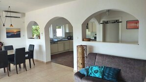 A living room with a sofa and chairs, a dining area with a table and chairs, and a kitchen visible through an archway. - SPACIOUS VILLA - OWN PRIVATE POOL, WIFI,  STUNNING SEA VIEWS (Bigova)