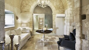 A room with a stone wall, a chandelier, a white sofa, a black armchair, and a round table with candles. - Wonderful Charming Villa with pool in the suggestive countryside near the sea, (RAGUSA)