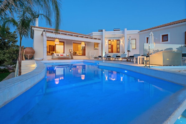 A poolside area with a clear pool, outdoor seating, and a building with a tiled roof.