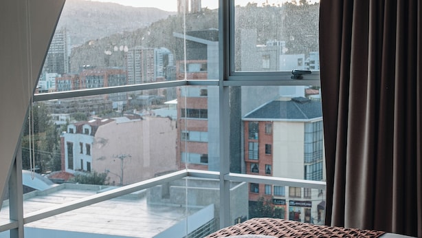 A hotel room with a large window offering a city view, a neatly made bed, and a view of the surrounding buildings. - Fratelli Aparthotel (La Paz)
